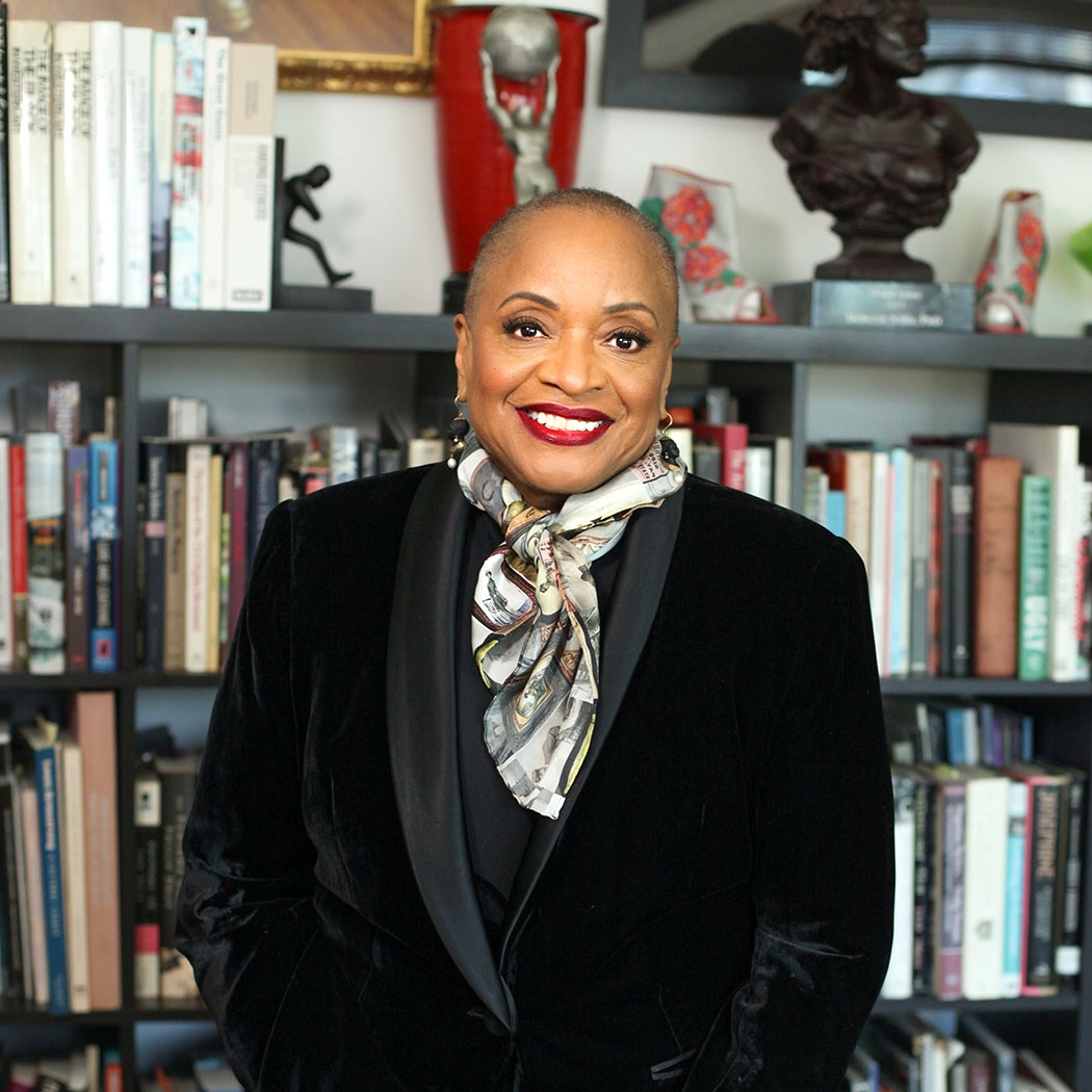 Gala Honoree Deborah Willis in a black blazer and multi-colored scarf in front of a bookshelf